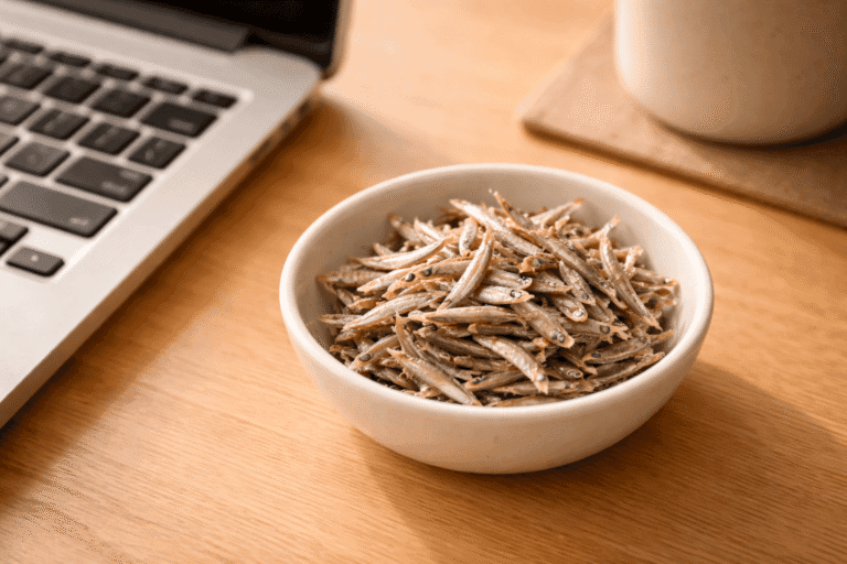 デスクのキーボード脇に置かれた白い器に盛られた小さなカタクチイワシ