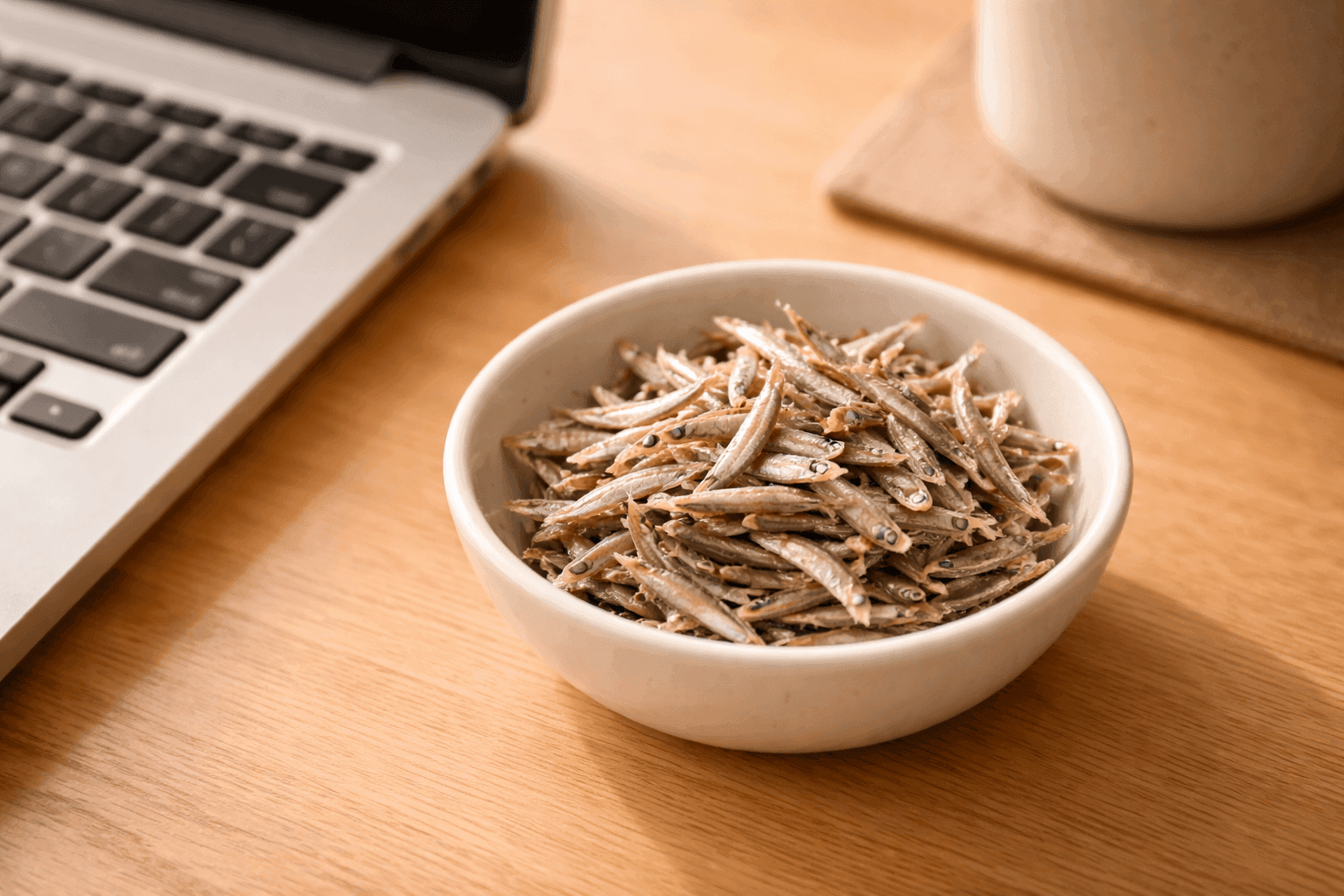 デスクのキーボード脇に置かれた白い器に盛られた小さなカタクチイワシ
